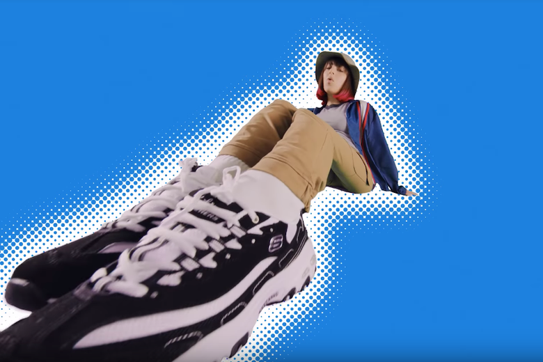 Charli XCX in skewed perspective with huge black and white sneakers close to the camera.